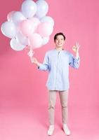 Young Asian man holding balloon on pink background photo