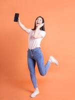 imagen completa de una joven asiática que usa un teléfono inteligente con fondo naranja foto