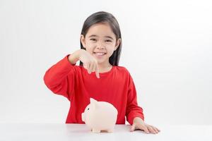 Little Asian girl saving money in a piggy bank, learning about saving, Kid save money for future education. Money, finances, insurance, and people concept photo