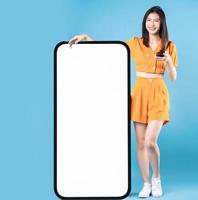 Full length photo of young Asian woman using smartphone on blue background