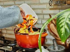 el chef arroja trozos de zanahorias de tres colores a una olla en la cocina foto