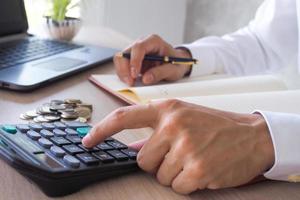 Asian businessmen work with calculators to calculate account information. In the office, work desks with documents and computers photo