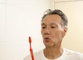 anciano mirando su viejo cepillo de dientes desgastado foto