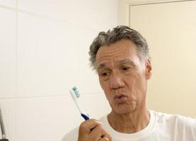 anciano mirando su viejo cepillo de dientes desgastado foto