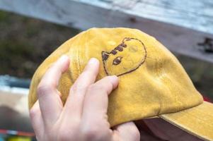 mano femenina sosteniendo un sombrero de bordado amarillo y una aguja trabajando en la costura de un patrón de gato en un proceso de trabajo manual. disfrutar del tiempo libre los fines de semana. foto