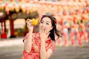 Young Asian woman wearing traditional cheongsam qipao dress holding ancient gold money in Chinese Buddhist temple. Celebrate Chinese lunar new year, festive season holiday. Emotion Wow photo