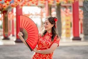 feliz Año Nuevo Chino. bella dama con traje tradicional cheongsam qipao sosteniendo un ventilador en el templo budista chino. foto