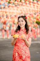 Vertical pictire. Happy Chinese new year. A young lady wearing traditional cheongsam qipao dress holding ancient gold money and orange fresh in Chinese Buddhist temple. photo