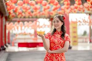 Happy Chinese new year. Asian woman wearing traditional cheongsam qipao dress holding ancient gold money in Chinese Buddhist temple. Celebrate Chinese lunar new year, festive season holiday. photo