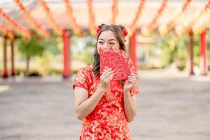 Portrait Young lady wearing traditional cheongsam qipao costume holding ang pao, red envelopes in Chinese Buddhist temple. Celebrate Chinese lunar new year, festive season holiday. photo