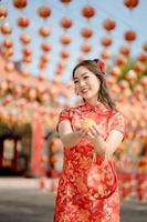 Vertical pictire. Happy Chinese new year. A young lady wearing traditional cheongsam qipao dress holding ancient gold money and bag in Chinese Buddhist temple. Celebrate Chinese lunar new year. photo