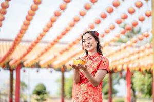 Beautiful Asian woman wearing traditional cheongsam qipao costume holding ancient gold money in Chinese Buddhist temple. Chinese New Year concept. Emotion smile photo