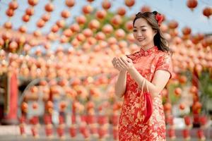 feliz Año Nuevo Chino. hermosa mujer asiática con vestido tradicional cheongsam qipao con dinero de oro antiguo y bolsa en el templo budista chino. celebrar el año nuevo lunar chino. foto