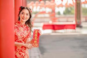 Happy Chinese new year. Asian woman wearing traditional cheongsam qipao dress holding blessing fortune card in Chinese Buddhist temple. Chinese text means blessed by a lucky star. Emotion Smile photo