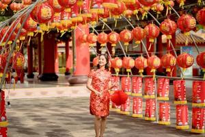 Beautiful lady wearing traditional cheongsam qipao dress holding lantern and walk while visiting the Chinese Buddhist temple. Celebrate Chinese lunar new year, festive season holiday. photo