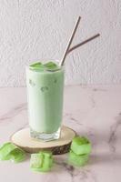 A transparent tall glass with organic cold green matcha tea and ice cubes, with eco-friendly metal straw on a wooden natural podium. front view. photo