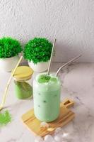 Iced tea matcha latte in a modern glass in the shape of a beer can with straw and ice in the shape of a ball stands on a wooden board. photo