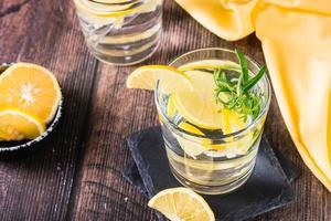 Pieces of lemon in a glass of water and rosemary on a wooden table. Detox drink photo