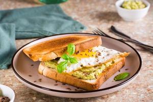 Sandwich with avocado, fried egg and flax seeds on toast on a plate on the table.