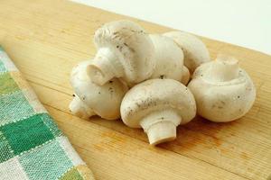 Small stack of white button mushrooms on a wooden cutting board photo