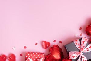 caja de regalo, velas y globos con forma de corazón rojo sobre fondo rosa. fondo romántico del día de san valentín con espacio de copia foto