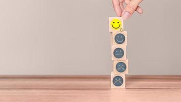 Hand putting a wooden cube block with a smile face icon on wood table. Concept of customer services best excellent business rating experience and testimonial. photo