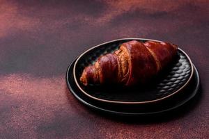 Delicious crispy croissant with chocolate on a black ceramic plate photo