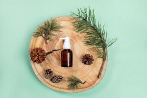 Top view small glass bottle with essential pine oil, branches, cones on wooden saw cut on mint green backdrop. photo