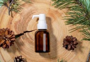 Small glass bottle with dispenser of spa aromatic essential pine oil, green branches, cones on wooden saw cut close up. photo