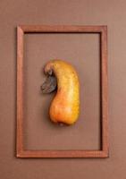 One ugly crooked ripe pear inside wooden frame on brown background. Vertical orientation. photo