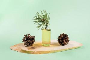 Essential pine oil in glass bottle with cones on wooden saw cut on mint green. photo