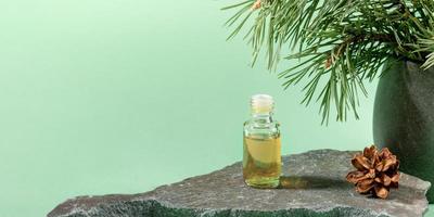 Glass bottle of essential pine oil on grey stone on mint green. Advertising banner. photo