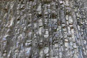 Natural grey layered stony mountain wall with uneven surface as background. photo