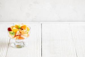 Glass bowl with fruit salad is standing on white wooden table. photo