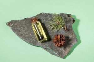 Essential pine oil in glass bottle with cone and twig on grey stone granite on mint green. Top view. photo