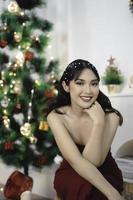 Portrait of pretty young girl cozy sit down, smiling wear red gown in decorated Christmas living room indoors photo