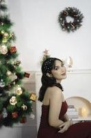 retrato de una joven bonita y acogedora sentada, sonriente, vestida de rojo en una sala de estar navideña decorada en el interior foto