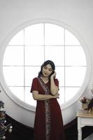 Portrait of a pretty young girl wearing a red gown, smiling at the camera, standing in decorated Christmas living room indoors photo