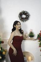 retrato de una linda joven con un vestido rojo, sonriendo a la cámara, de pie en un salón de Navidad decorado en el interior foto