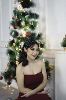 retrato de una joven bonita y acogedora sentada, sonriente, vestida de rojo en una sala de estar navideña decorada en el interior foto
