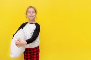 little girl in pajamas and with a pillow on a yellow background with copy space photo