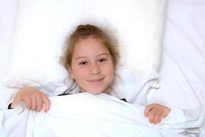 niña acostada en la cama cubierta con una manta foto