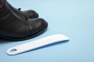 black boots and a shoe horn on a blue background with copy space photo