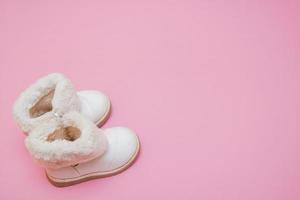 children's white fur boots on a pink background with copy space photo