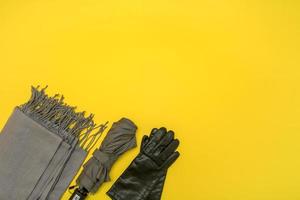 gray scarf and gray umbrella with gloves on yellow background with copy space photo