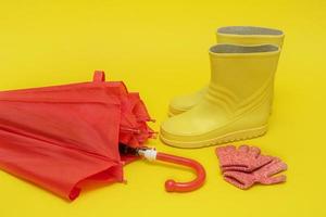 red children's umbrella, boots and gloves on a yellow background with copy space photo