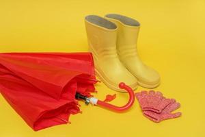 red children's umbrella, boots and gloves on a yellow background with copy space photo