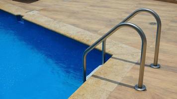 esquina de una piscina con borde de mármol, paredes de cerámica azul y escalera de piscina foto