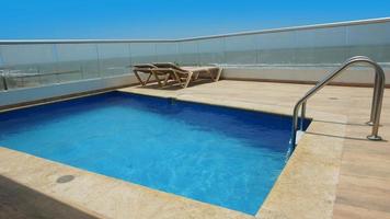 Swimming pool with marble border, blue ceramic walls and pool ladder with sea in background photo