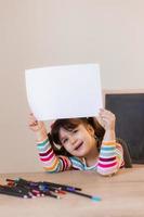 a cute little girl in a drawing lesson holds an empty white sheet in her hands, a space for text. Children and creativity. High quality photo